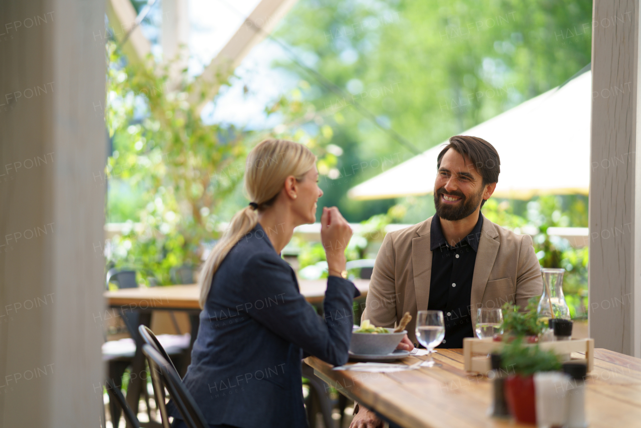 Couple sitting outdoors on terrace restaurant, having romantic dinner date. Business lunch for two managers, discussing new business project.