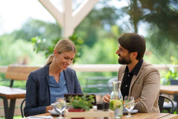 Business lunch for two managers, discussing new business project. Couple sitting outdoors on terrace restaurant, having romantic dinner date.