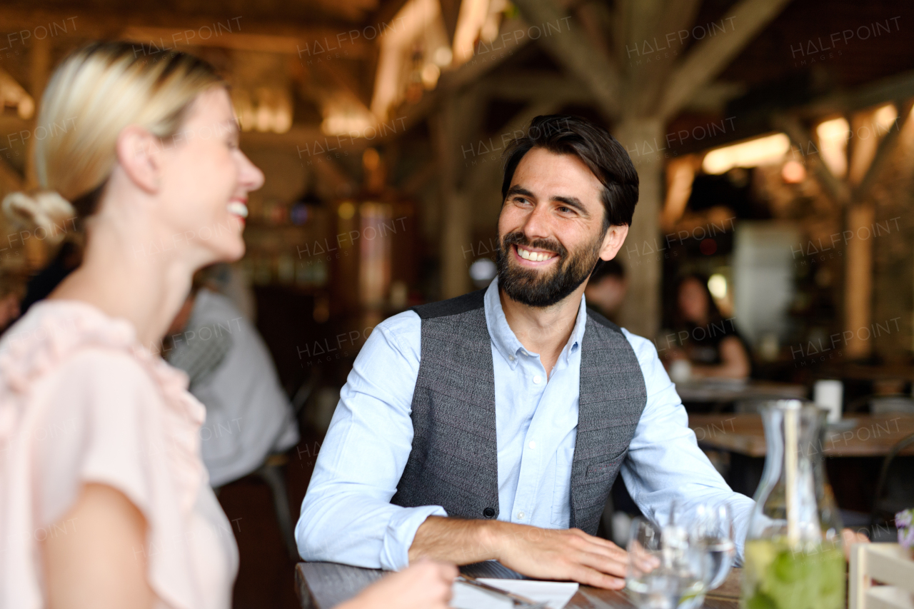 Happy loving couple at date in restaurant. Husband and wife sitting at table, laughing, having brunch, lunch in modern cafe.