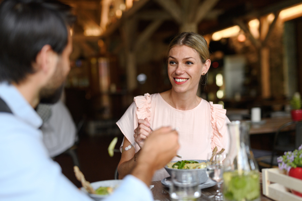 Happy loving couple at date in restaurant. Husband and wife sitting at table, laughing, having brunch, lunch in modern cafe.