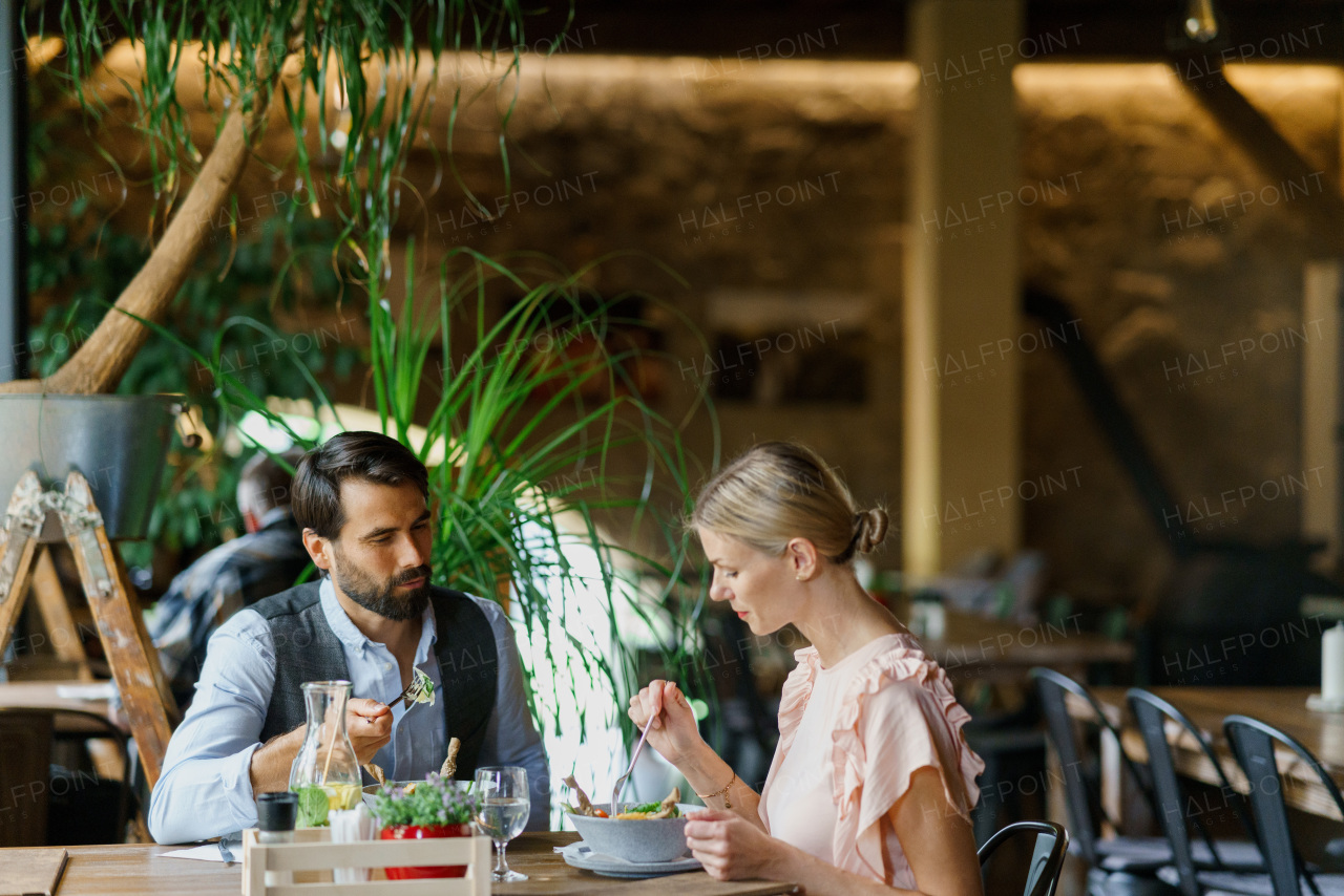 Happy loving couple at date in restaurant. Husband and wife sitting at table and talking, having brunch, lunch in modern cafe.