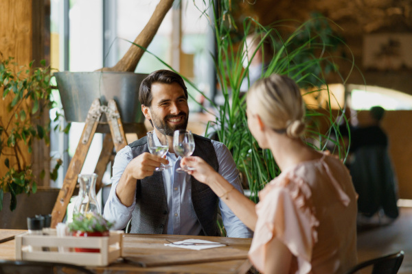 Happy loving couple at date in restaurant. Husband and wife sitting at table, clinging with glasses, having brunch, lunch in modern cafe.