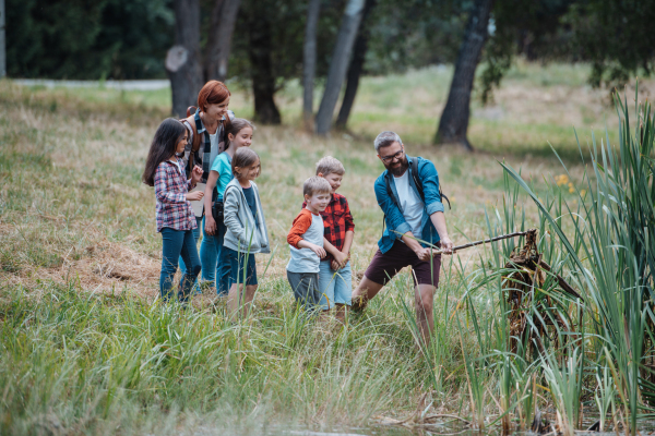 Teacher showing decaying water, lake plants to school children, during field teaching class. Outdoor active education helping young student to learn about ecosystem, nature.