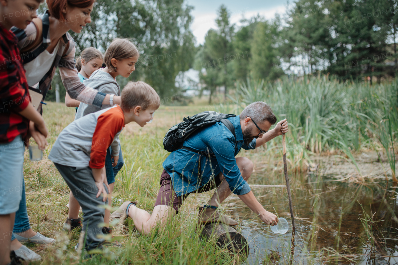 Teacher showing lake water to school children, during field teaching class. Outdoor active education helping young student to learn about ecosystem, nature.