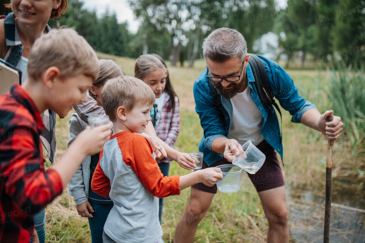 Teacher showing lake water to school children, during field teaching class. Outdoor active education helping young student to learn about ecosystem, nature.