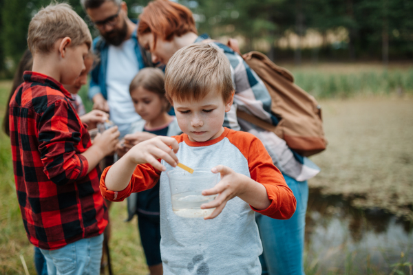 Young students analyzing water quality, ph level with indicator strips during biology field teaching class. Female teacher during outdoor active education about ecosystem, nature.