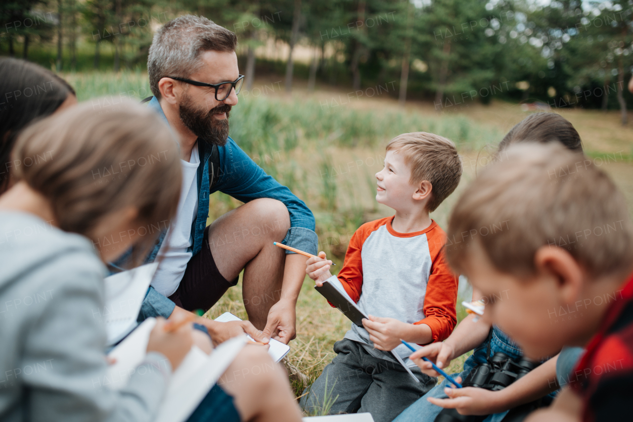 Young students learning about nature, forest ecosystem during biology field teaching class, writing notes. Teachers talking with children during outdoor active education. Teachers day.