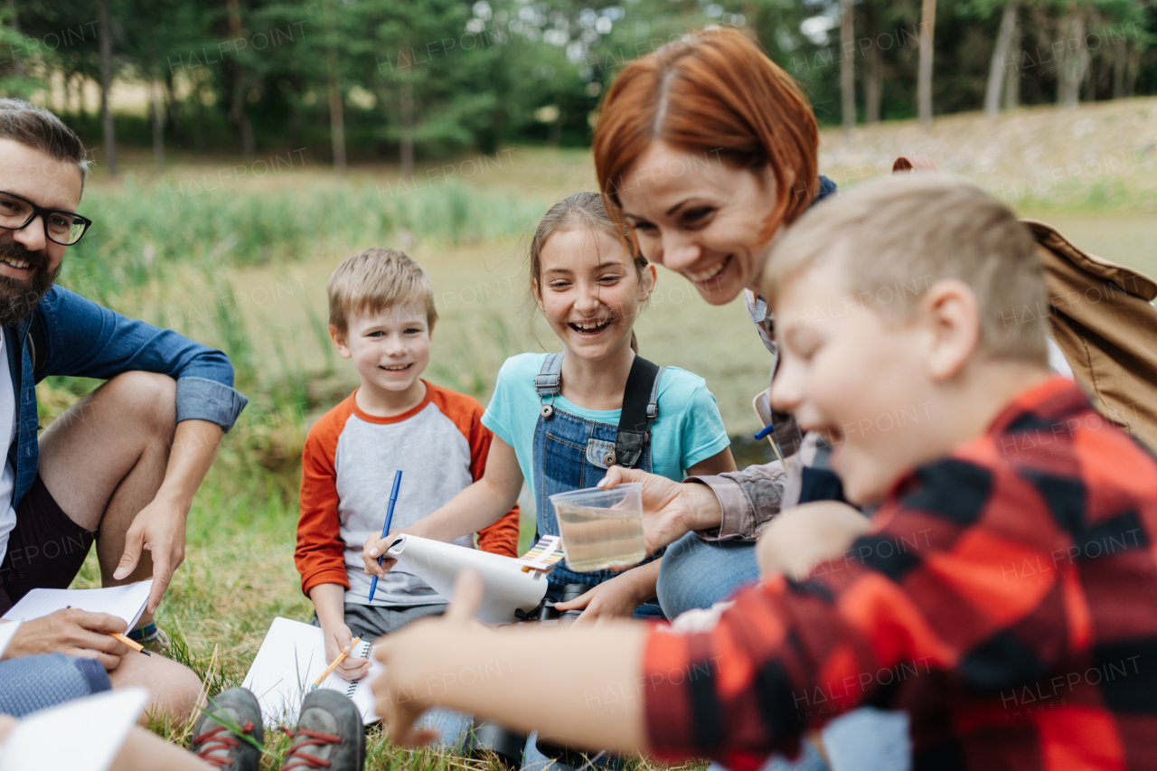 Young students analyzing water quality, ph level with indicator strips during biology field teaching class. Female teacher during outdoor active education about ecosystem, nature.