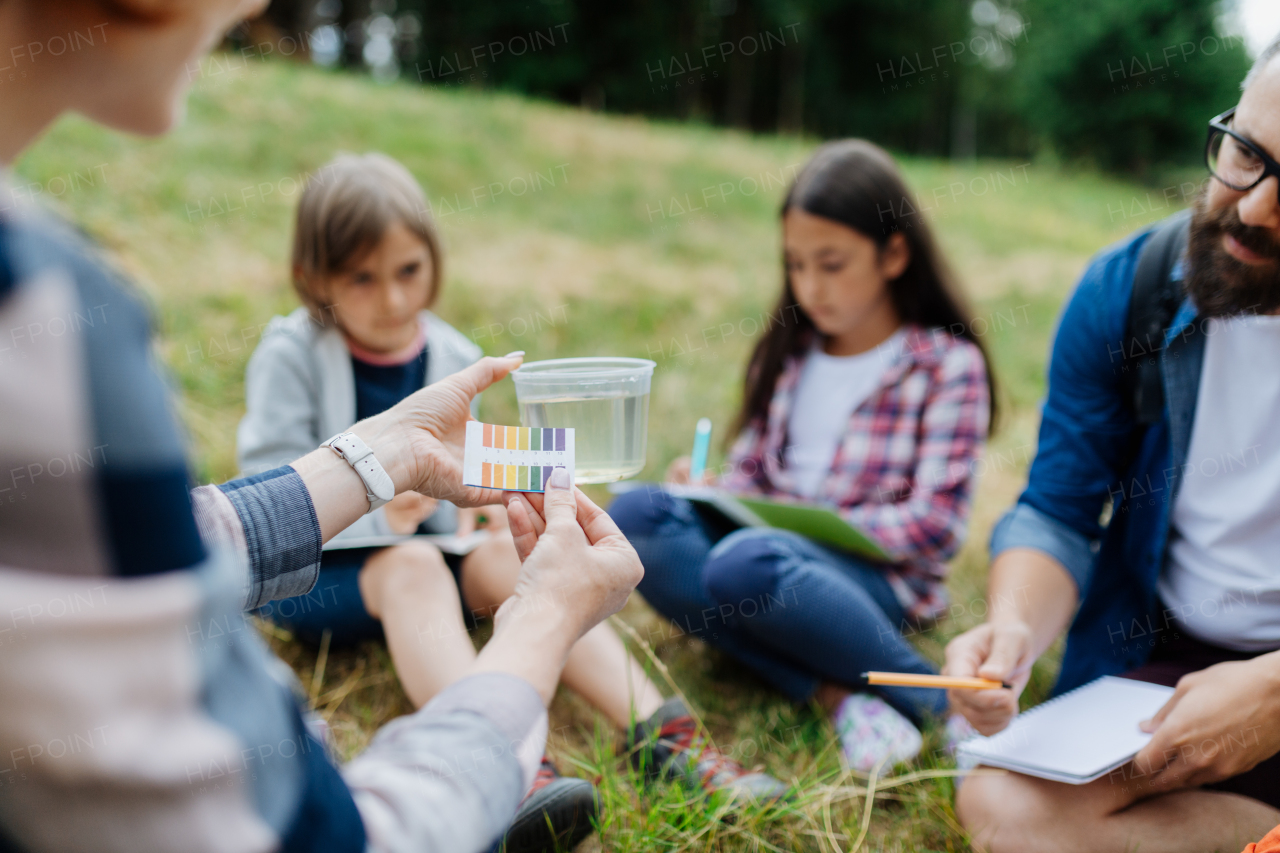 Young students analyzing water quality, ph level with indicator strips during biology field teaching class. Female teacher during outdoor active education about ecosystem, nature.