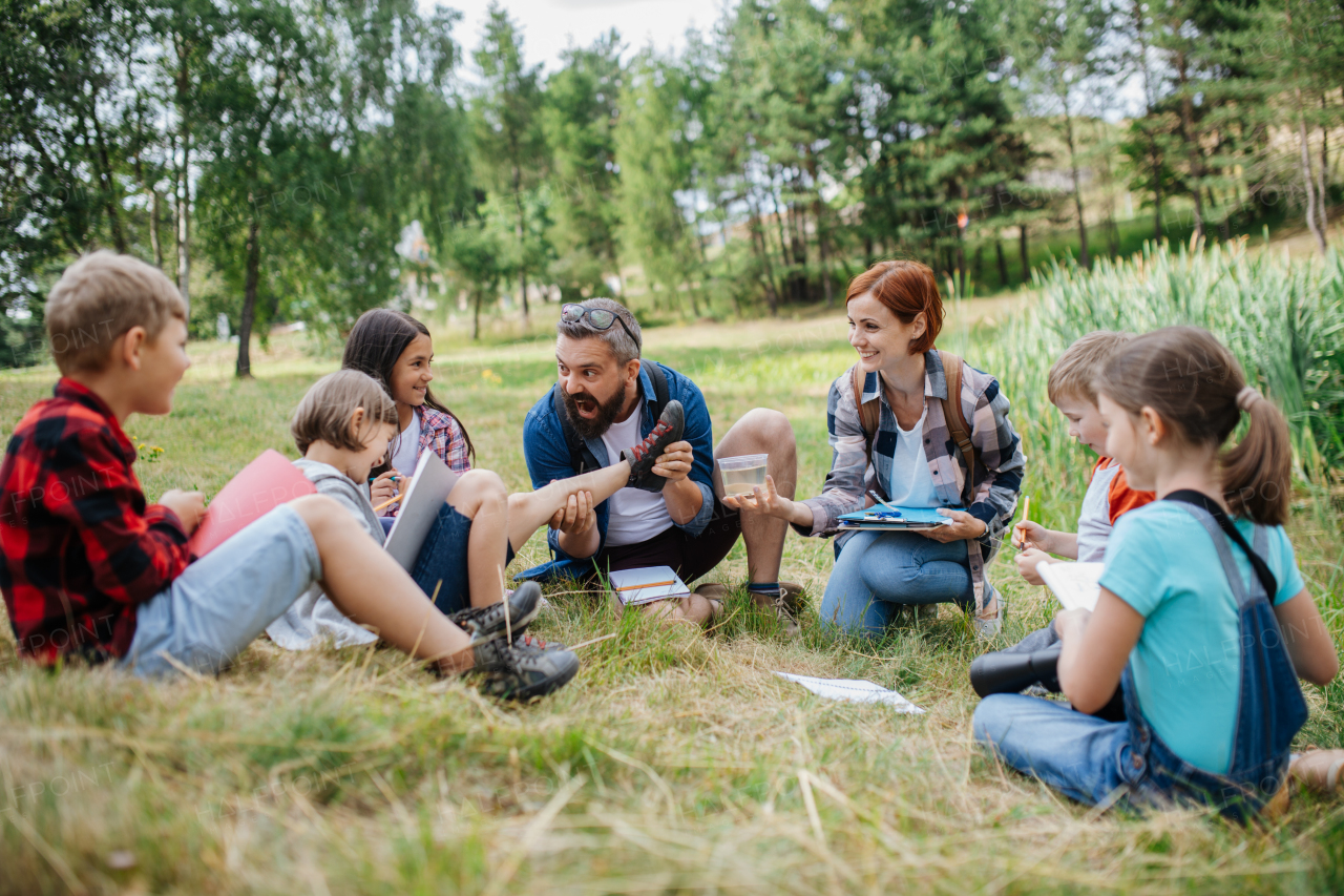 Young students analyzing water quality, ph level with indicator strips during biology field teaching class. Female teacher during outdoor active education about ecosystem, nature.