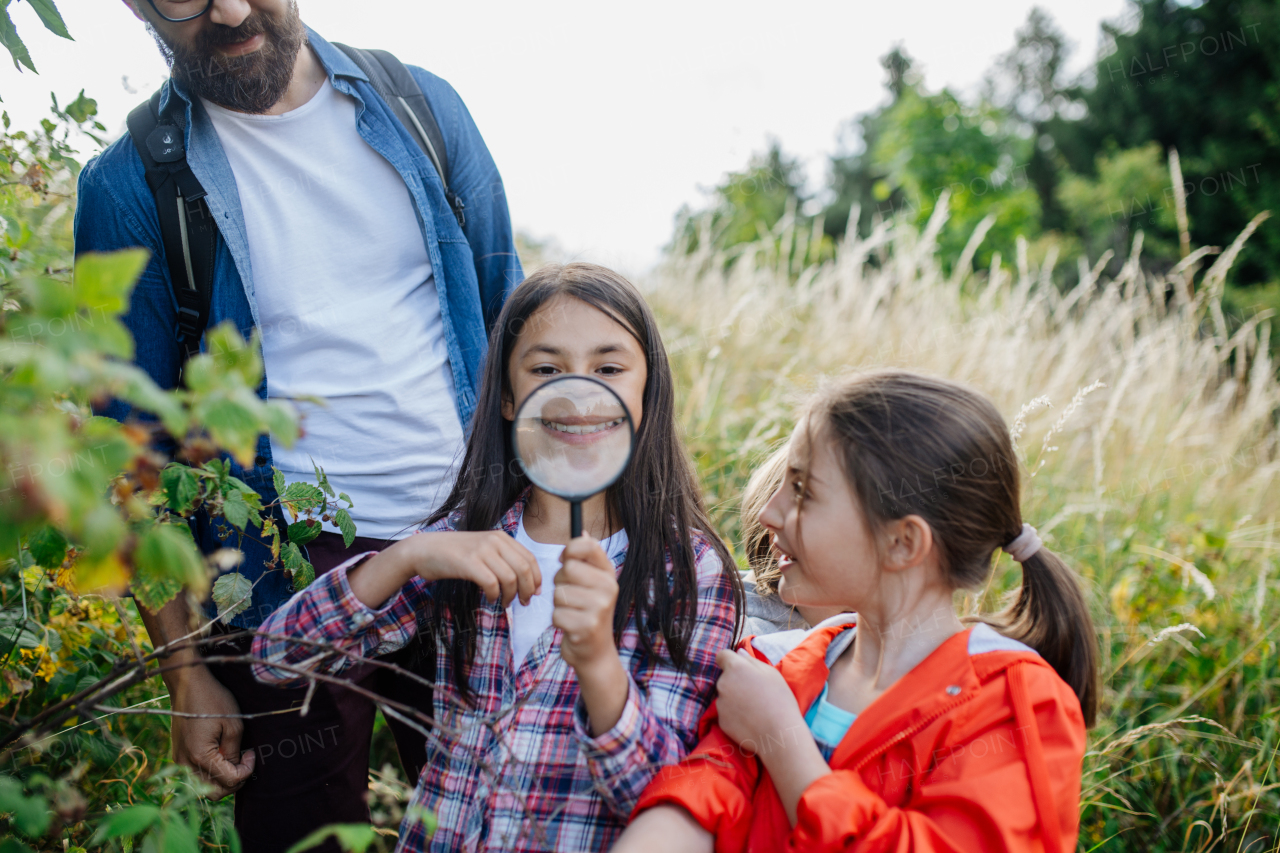 Young students learning about nature, forest ecosystem during biology field teaching class, observing wild plants with magnifying glass. Dedicated teachers during outdoor active education. Teachers' Day.