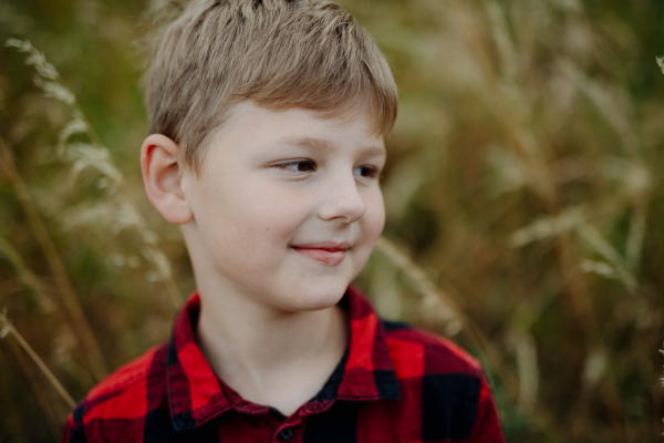 Portrait of young boy standing in nature, in the middle of tall grass with closed eyes, headshot. Copy space.