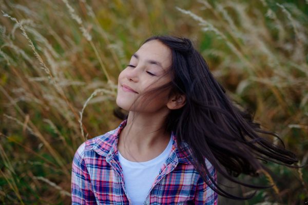 Portrait of beautiful young girl standing in nature, in the middle of tall grass with closed eyes, headshot. Copy space.