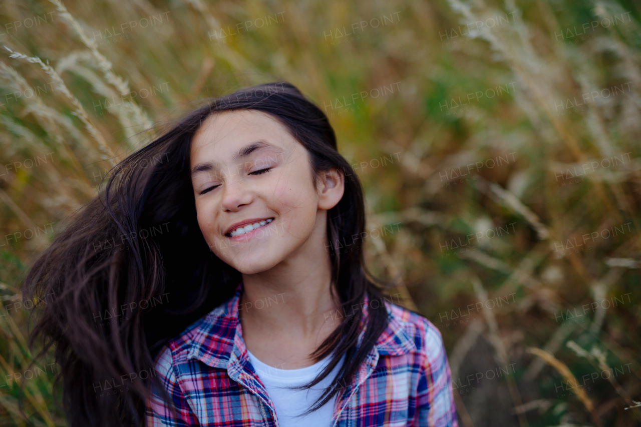 Portrait of beautiful young girl standing in nature, in the middle of tall grass with closed eyes, headshot. Copy space.