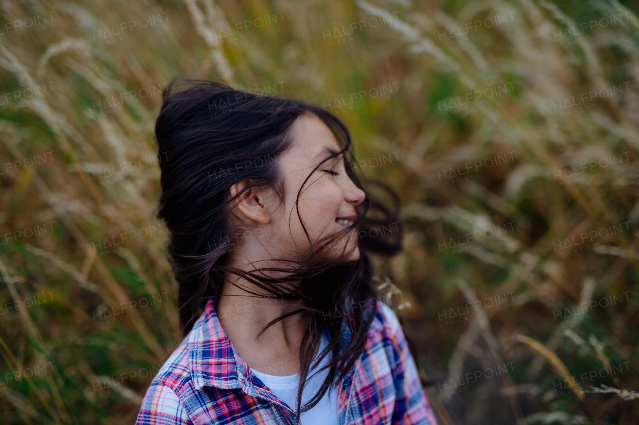 Portrait of beautiful young girl standing in nature, in the middle of tall grass with closed eyes, headshot. Copy space.