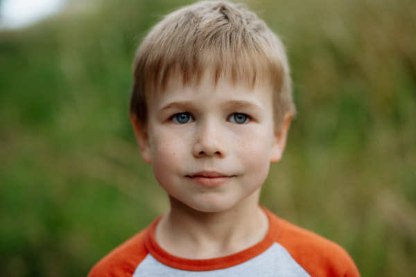 Portrait of young boy standing in nature, in the middle of tall grass with closed eyes, headshot. Copy space.