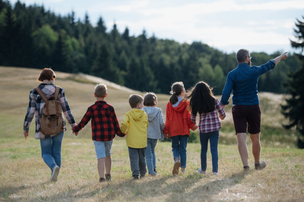 Young students walking across meadow during biology field teaching class, holding hands. Dedicated teachers during outdoor active education teaching about ecosystem and nature.