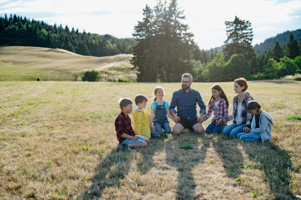 Children and teachers sitting on grass on meadow playing clapping game. Dedicated teachers during outdoor active education teaching about ecosystem, ecology and nature.