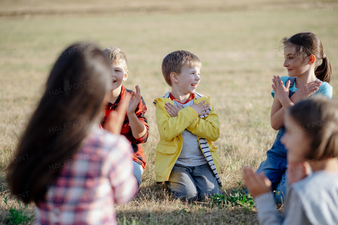 Children sitting on grass on meadow playing clapping game. Dedicated teachers during outdoor active education teaching about ecosystem, ecology and nature.