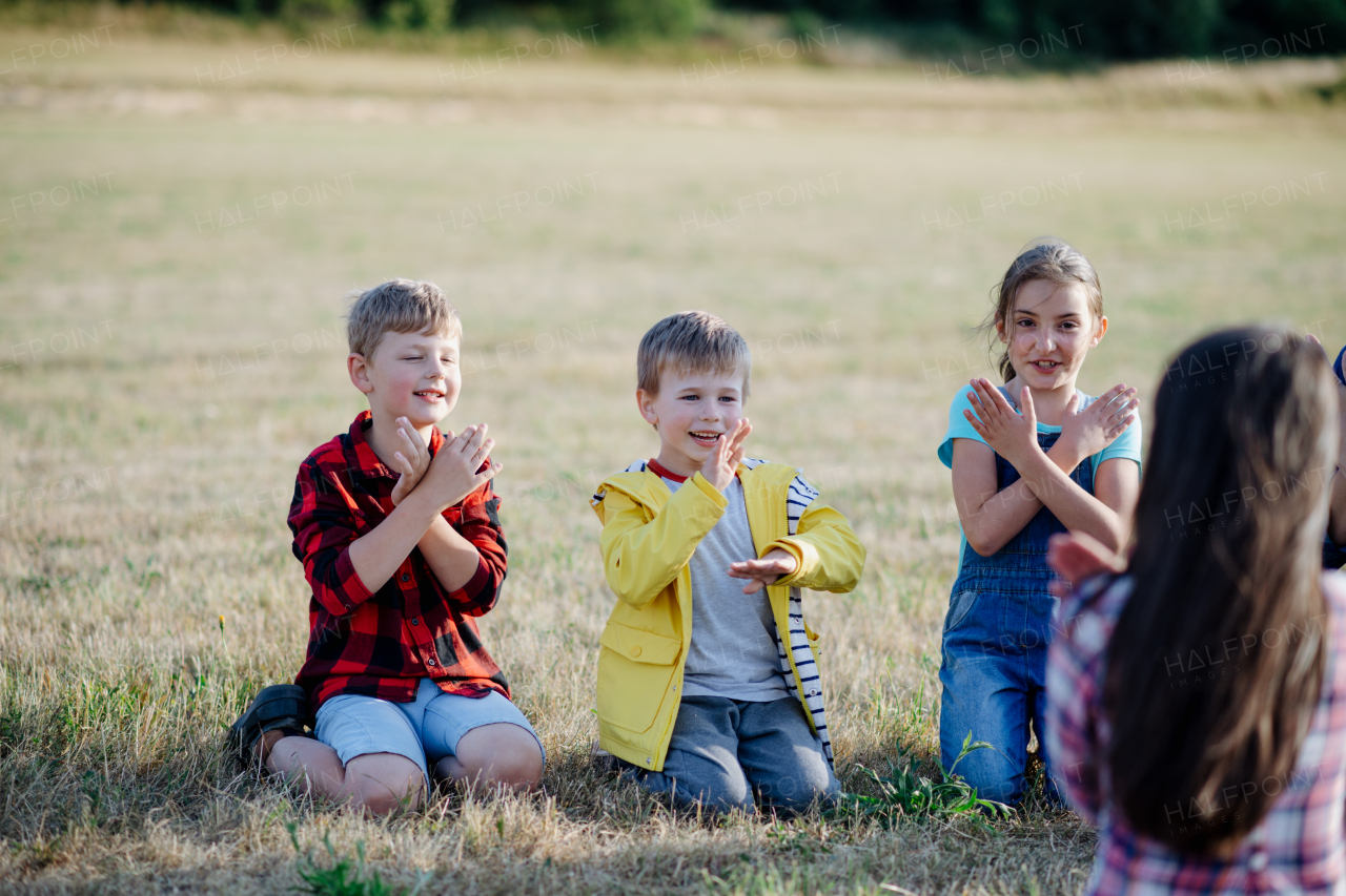 Children sitting on grass on meadow playing clapping game. Dedicated teachers during outdoor active education teaching about ecosystem, ecology and nature.