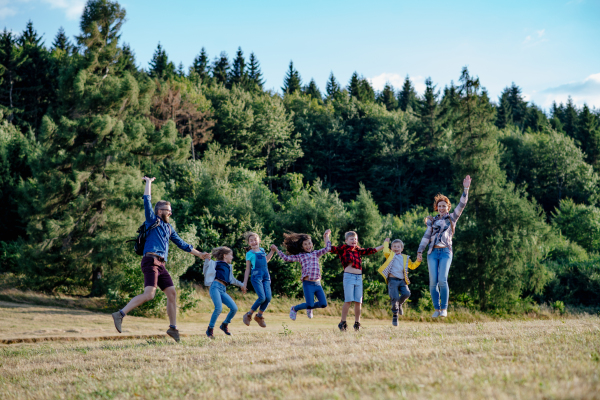 Young students walking across meadow during biology field teaching class, holding hands. Dedicated teachers during outdoor active education teaching about ecosystem and nature.