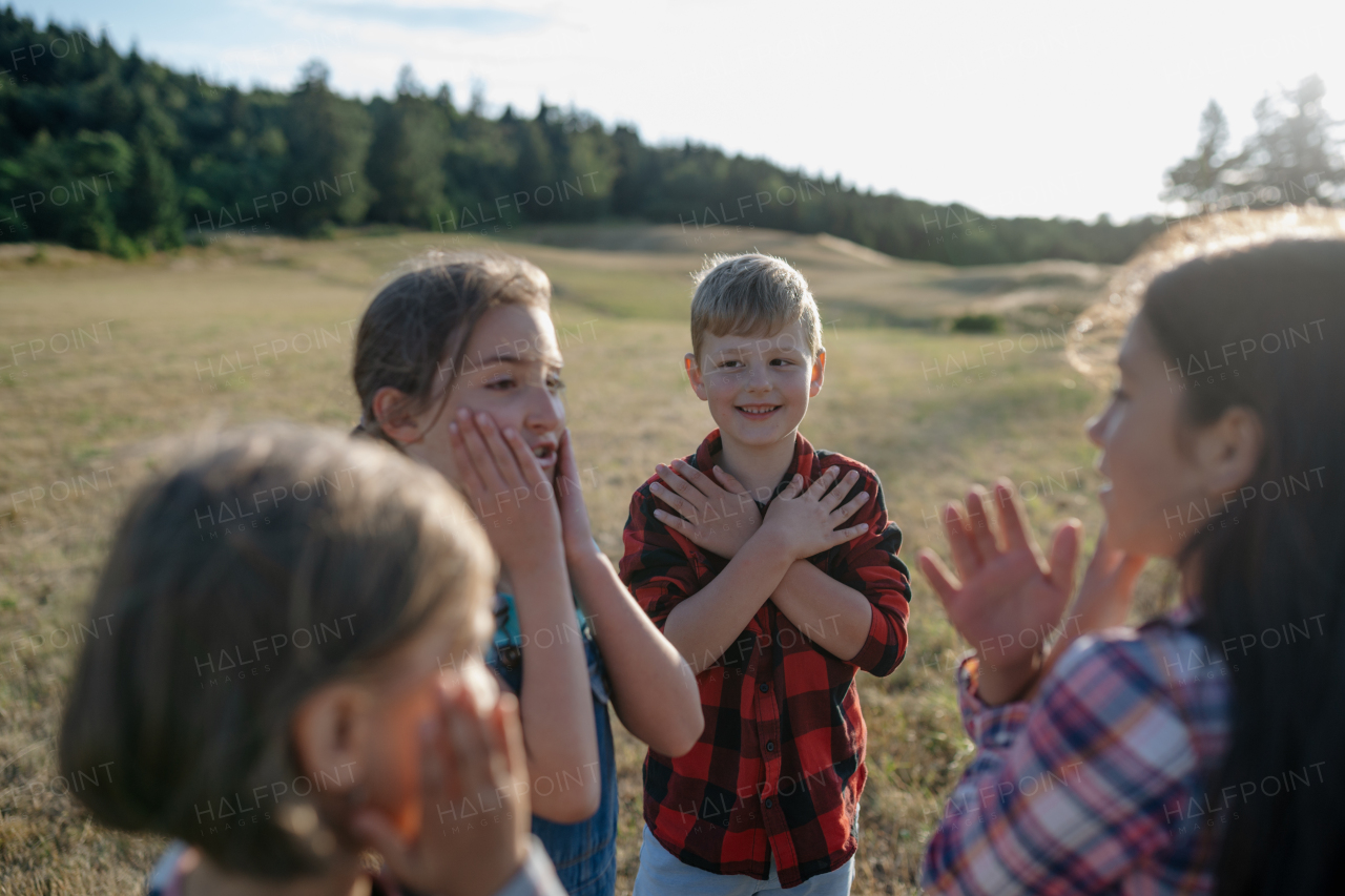 Portrait of young classmate playing hand clapping game outdoors. Students during field teaching class, standing in the middle of meadow, having fun. Learning about ecosystem, ecology.