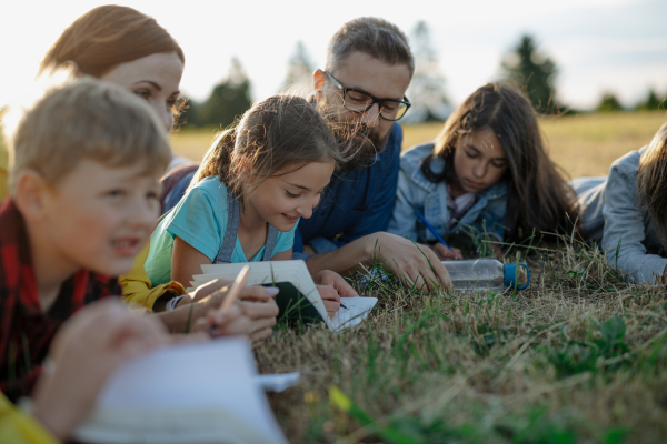 Young students learning about nature, forest ecosystem during biology field teaching class, writing notes. Teachers talking with children during outdoor active education. Teachers day.