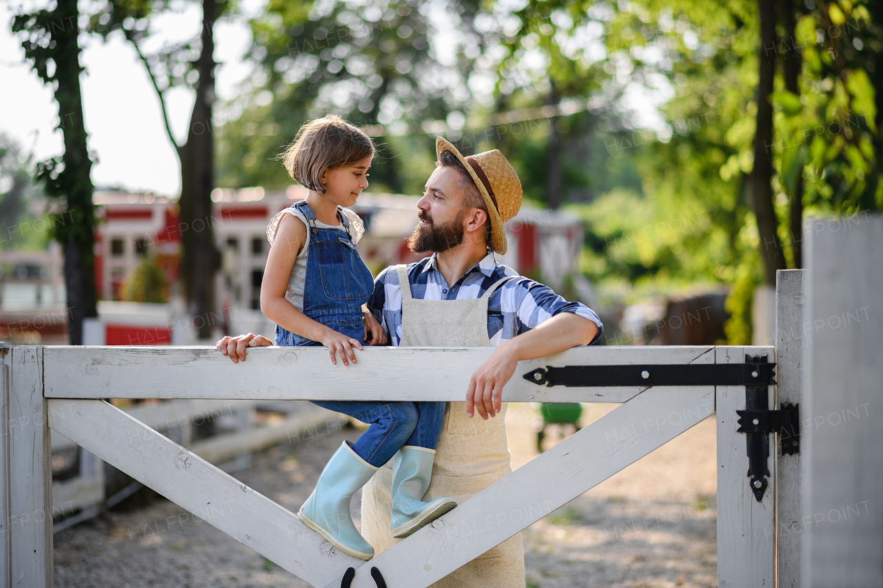 Portrait of farmer family, father with daughter sitting on wooden fence on family farm. Concept of multigenerational farming.