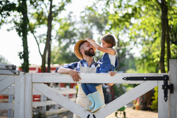 Portrait of farmer family, father with daughter sitting on wooden fence on family farm. Concept of multigenerational farming.