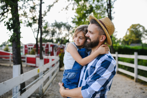 Portrait of a farmer family, father and young daughter standing on wooden fence on family farm. Concept of multigenerational farming.