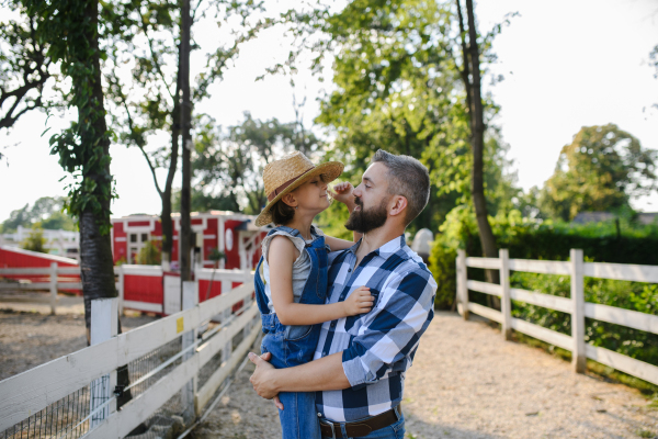 Portrait of a farmer family, father and young daughter standing on wooden fence on family farm. Concept of multigenerational farming.