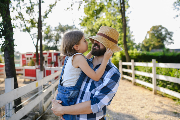 Portrait of a farmer family, father and young daughter standing on wooden fence on family farm. Concept of multigenerational farming.