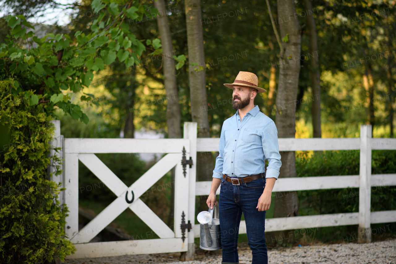 A portrait of handsome farmer holding watering can, working on family farm.