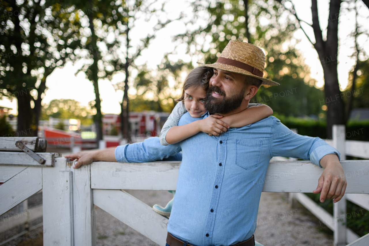 Portrait of a farmer family, father and young daughter standing on wooden fence on family farm. Concept of multigenerational farming.