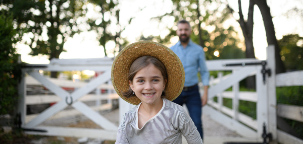 Portrait of a farmer family, father and young daughter standing on wooden fence on family farm. Concept of multigenerational farming.