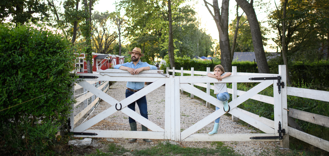 Portrait of a farmer family, father and young daughter standin on wooden fence on family farm. Concept of multigenerational farming.