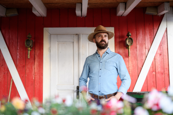 Portrait of handsome farmer standingon wooden patio at his farm. Man with hat working on family ranch.