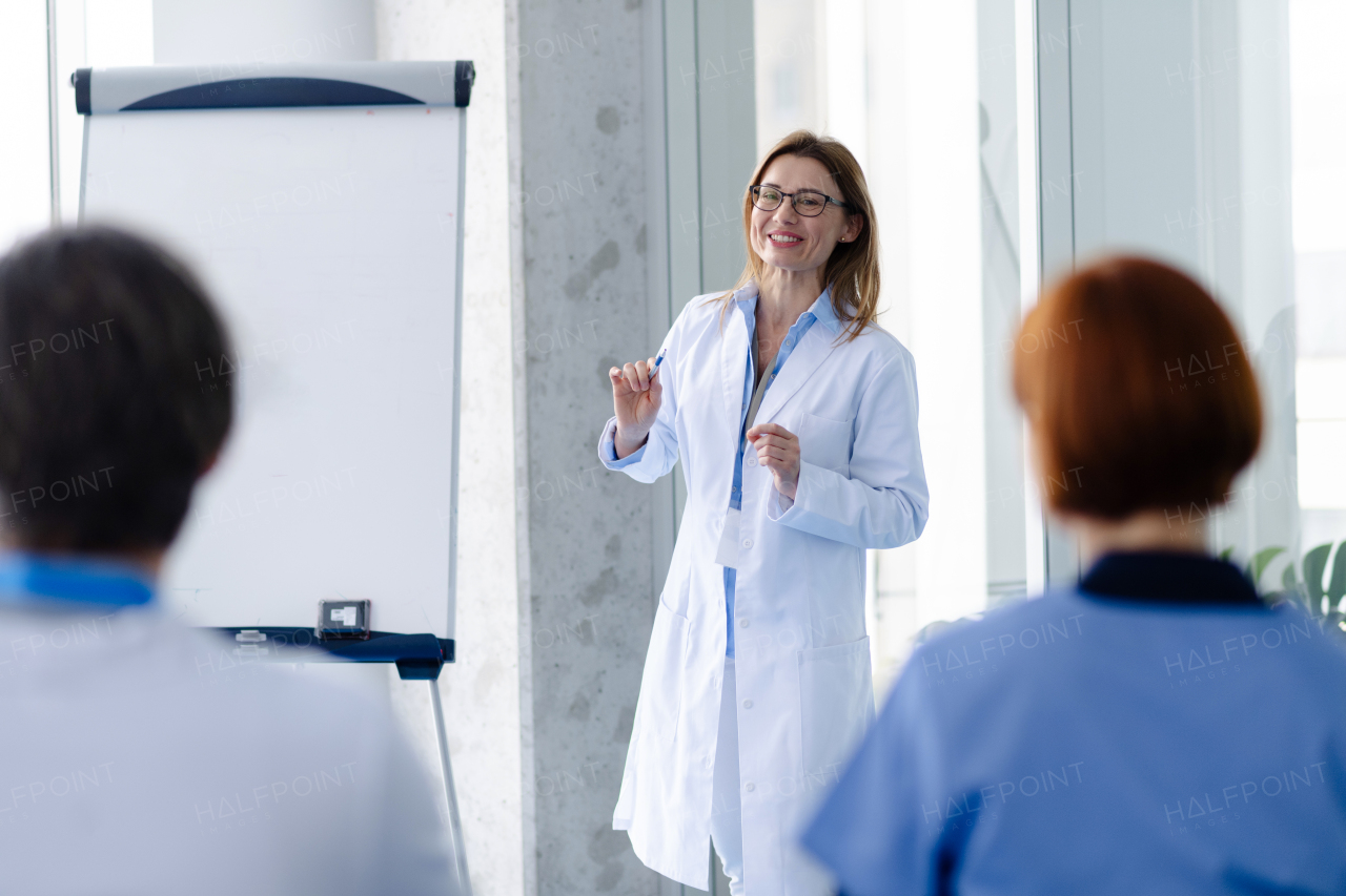 Female doctor as speaker at conference for group of healtcare workers, medical team sitting and listening presenter. Medical experts attending an education event, seminar in board room.