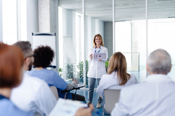 Female doctor as speaker at conference for group of healtcare workers, medical team sitting and listening presenter. Medical experts attending an education event, seminar in board room.