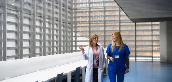 Two female doctors discussing test results, walking across corridor. Colleagues discussing patients diagnosis. Women in medicine science