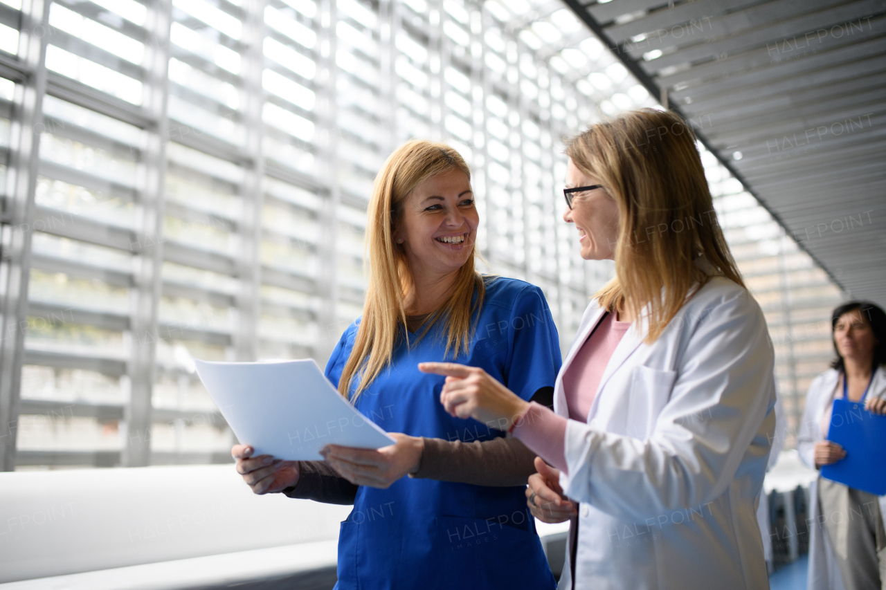 Two female doctors discussing test results, walking across corridor. Colleagues discussing patients diagnosis. Women in medicine science