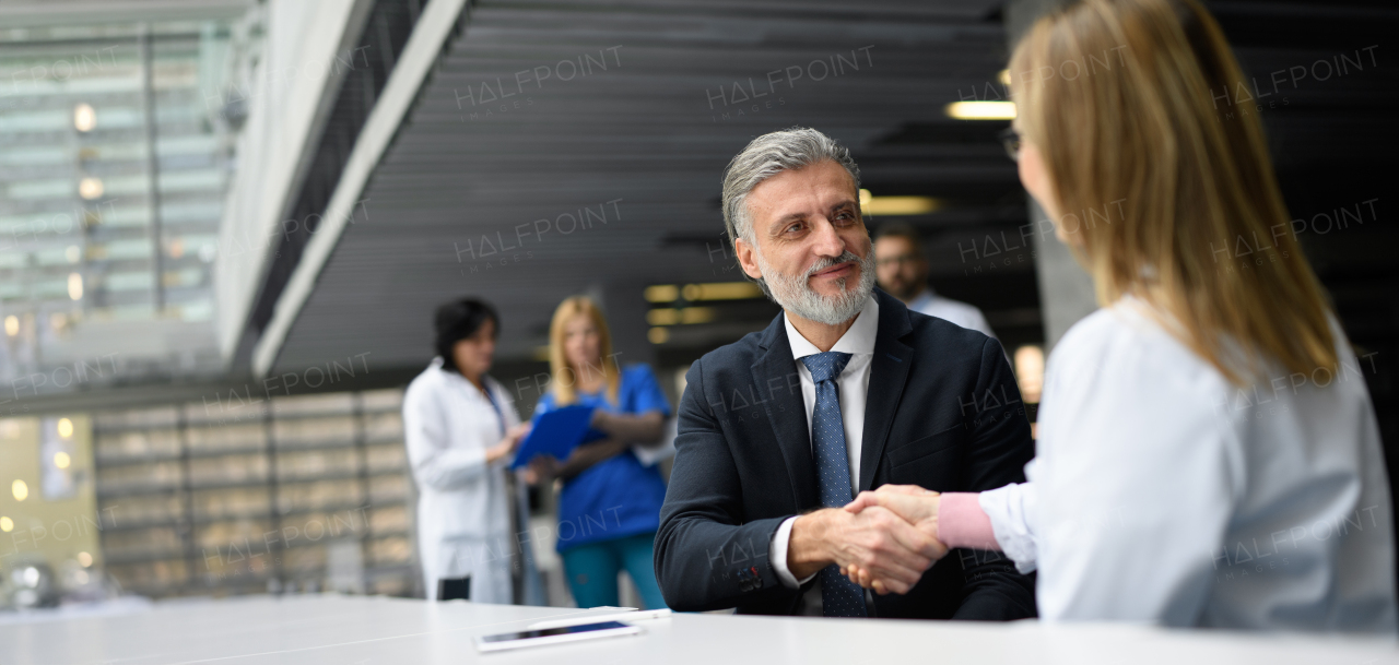 Doctors talking to pharmaceutical sales representative, shaking hands, presenting new pharmaceutical product. Hospital director, manager talking with female doctor. Banner with copyspace.