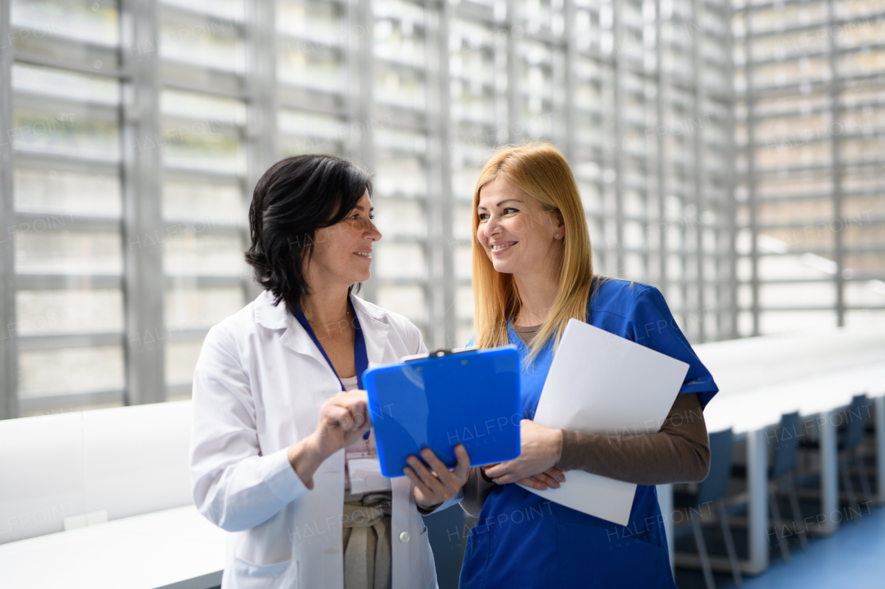 Two female doctors discussing test results, walking across corridor. Colleagues discussing patients diagnosis. Women in medicine science