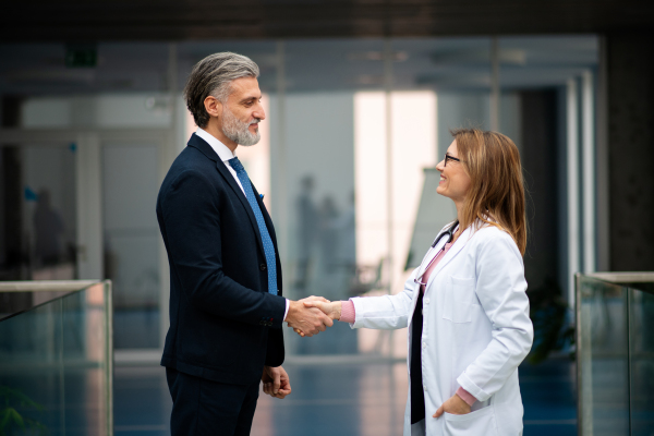 Doctors talking to pharmaceutical sales representative, shaking hands, presenting new pharmaceutical product. Hospital director, manager talking with female doctor. Side view with copyspace.