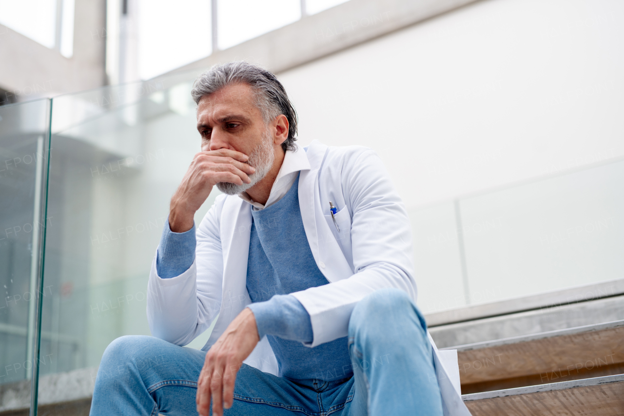 Serious and frustrated male doctor sitting on the hospital stairs. Burnout for healthcare workers.