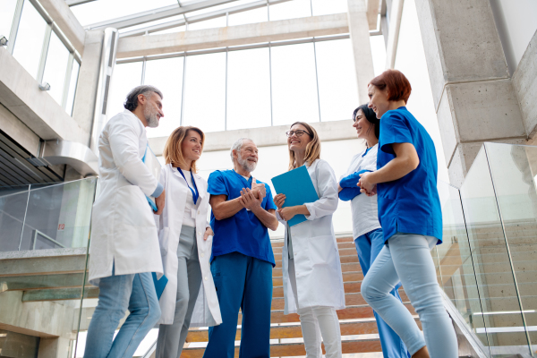 Team of doctors taking in hospital corridor, smiling. Colleagues, doctors team discussing patients diagnosis, standing on stairs. Low angle shot with copy space.