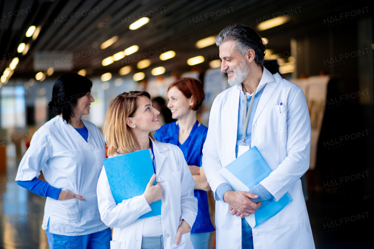 Team of doctors walking across hospital corridor, talking. Colleagues, doctors team discussing patients diagnosis.