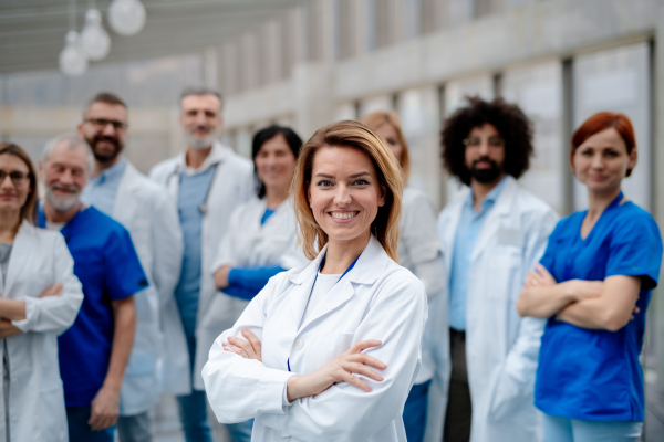 Portrait of beautiful female doctor standing in front of team of doctors. Healthcare team with doctors, nurses, professionals in medical uniforms in hospital, modern clinic.