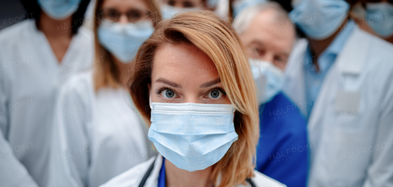 Portrait of beautiful female doctor with surgical mask standing in front of team of doctors. Healthcare team with doctors, nurses, professionals in medical uniforms and face masks in hospital, modern clinic.