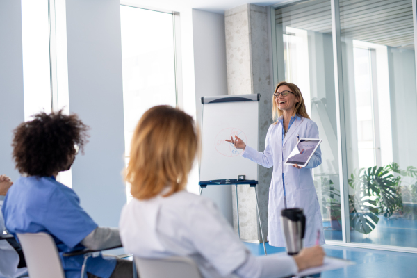 Female doctor as speaker at conference for group of healtcare workers, medical team sitting and listening presenter. Medical experts attending an education event, seminar in board room.